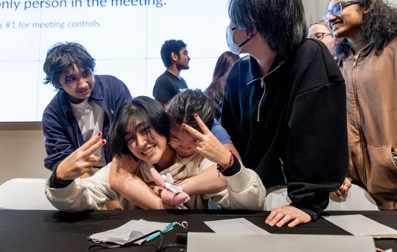 A high school student smiles at the camera while surrounded by others.