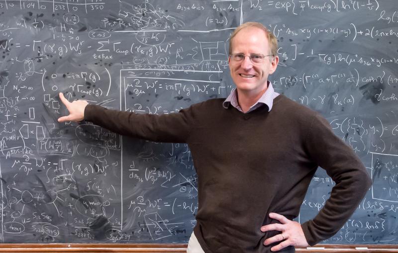 Lance Dixon pointing at mathematical formula on a chalkboard