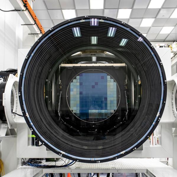 A digital camera sensor is visible through a large camera lens sitting inside a white room.