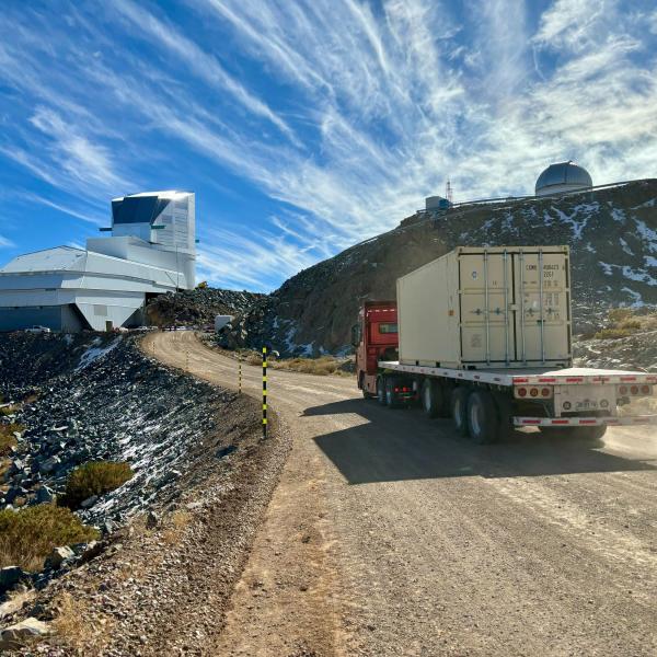 A semi truck traveling a gravel road approaches two large telescope facilities.