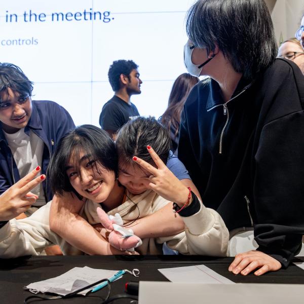 A high school student smiles at the camera while surrounded by others.