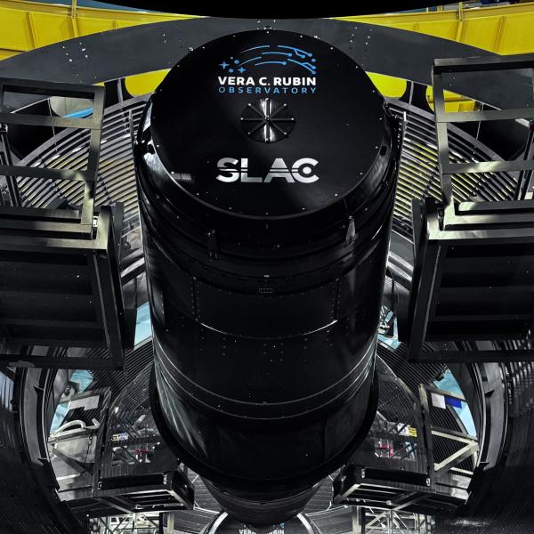 A large black cylindrical camera is positioned in a telescope dome.